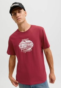 Camiseta de algodón color marrón con un diseño gráfico blanco que incluye el texto "Jack & Jones" y "Originals". Mangas cortas y un corte clásico.