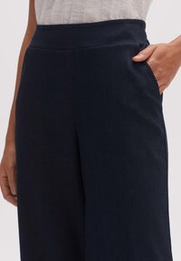 Námořnické modré kalhoty s širokým střihem, texturovaným povrchem, vysokým pasem a bočními kapsami. Materiál se zdá být lehký a mírně zmačkaný.