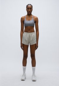 Αθλητικό σουτιέν σε γκρι με υφή με σχέδιο, σε συνδυασμό με ελαφριά μπεζ σορτς. Το μοντέλο φορεί λευκές κάλτσες και αθλητικά παπούτσια, στέκεται σε ουδέτερο φόντο.