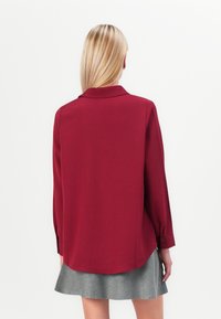 Μαρολί πουκάμισο με μακριά μανίκια και γιακά, με απαλό υφή. Το στρίφωμα είναι ελαφρώς καμπυλωτό, με κουμπωτές μανσέτες. Συνδυάζεται με γκρι φούστα.