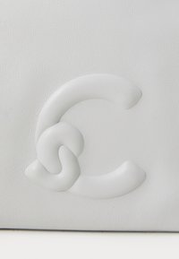 Borsa a mano in pelle bianca con un design del logo in rilievo a motivo ripetuto. La texture è liscia con dettagli di grana sottili.