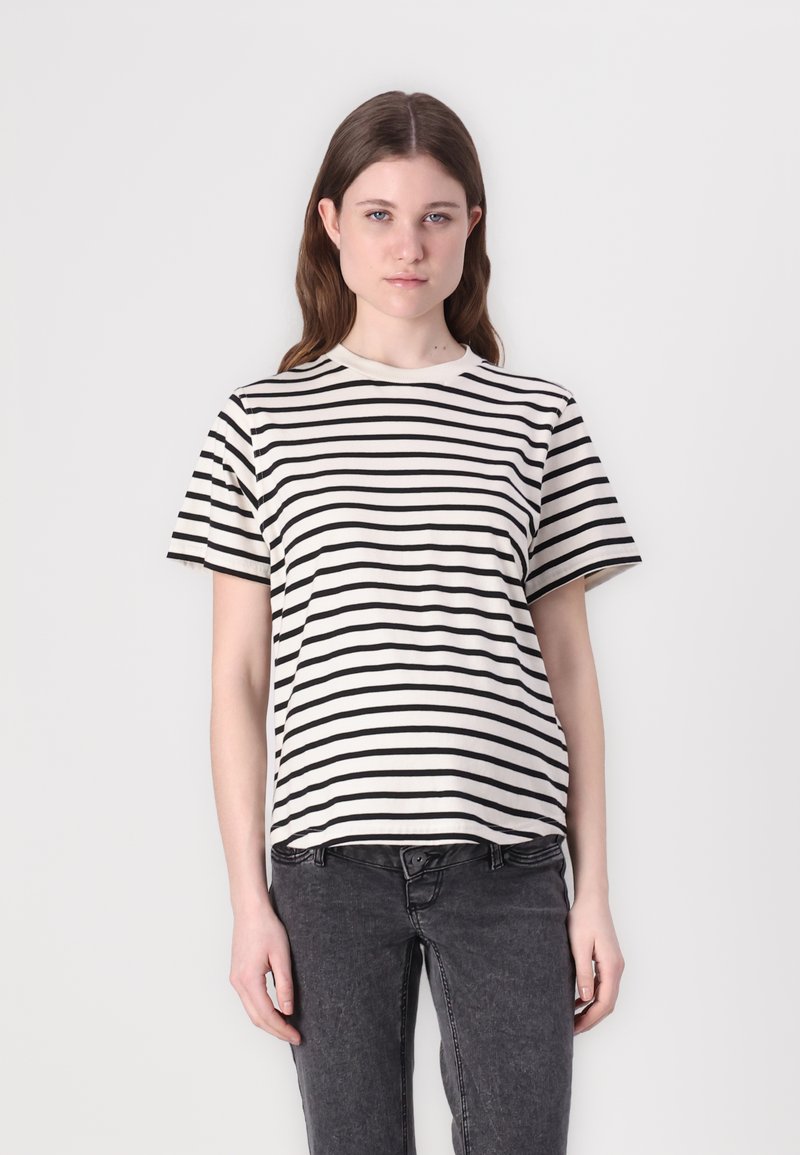 Tricou rayé în crem și negru, cu mâneci scurte, guler rotund, din material de bumbac. Modelul îl poartă cu blugi gri închis.