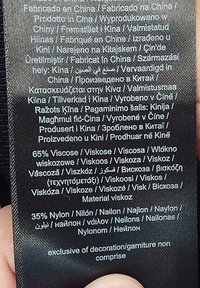 Czarna metka pielęgnacyjna z tkaniny zawierająca wiele języków. Tekst zawiera "65% wiskoza" oraz "35% nylon". Informacje o produkcji: "Wyprodukowano w Chinach".