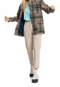 Brązowa i zielona kurtka w kratę z zatrzaskami, niebieska bluzka, kremowe spodnie z kordurowej tkaniny oraz beżowe buty na platformie z czarnymi podeszwami.
