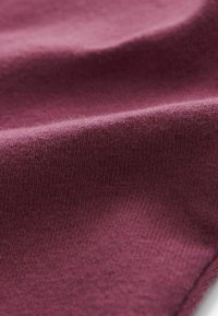 Textúrovaná tkanina v hlbokej burgundskej farbe, s jemným ryhovaným vzorom. Povrch vyzerá mäkký a trochu nadýchaný.