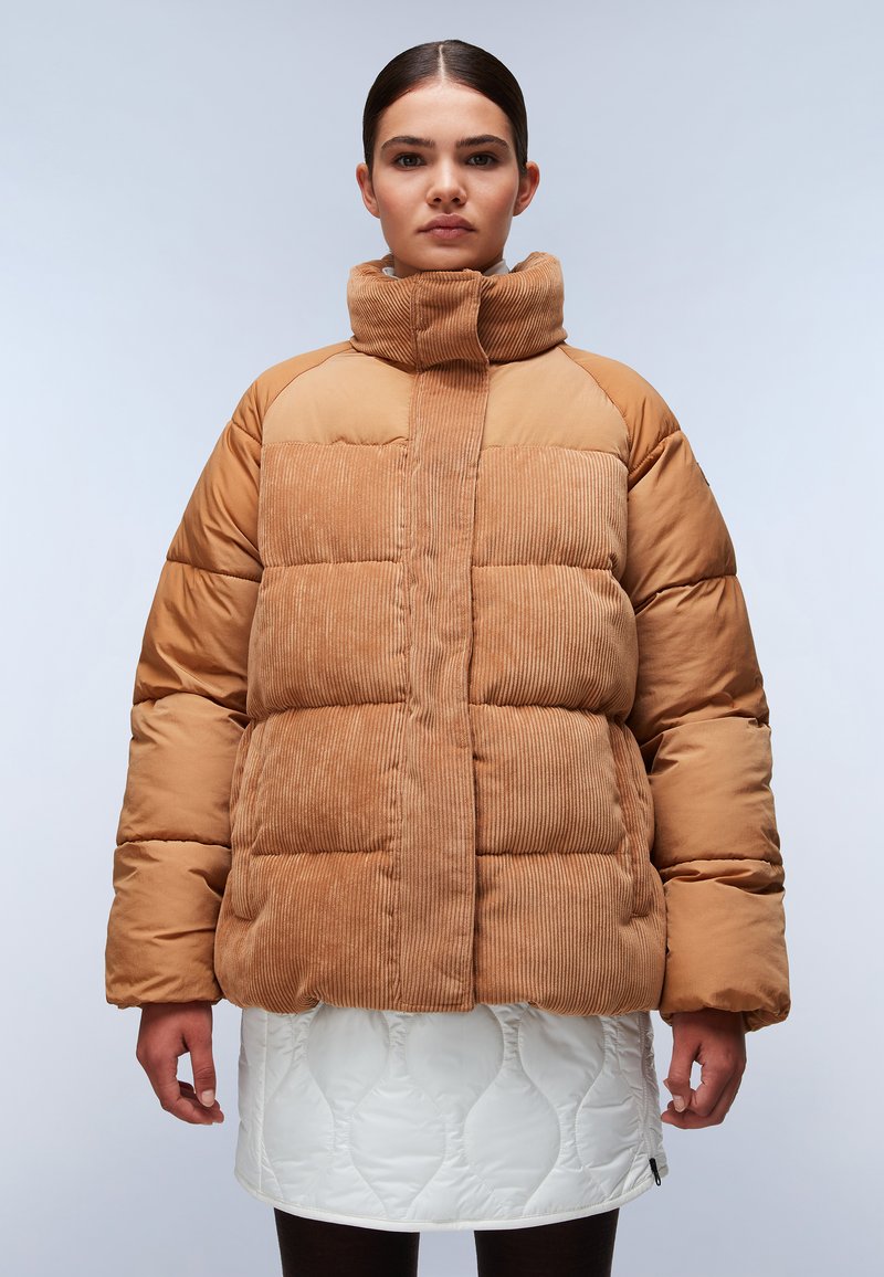 Brązowa kurtka puchowa z teksturą w prążki i wysokim kołnierzem. Nosi ją modelka na białej, pikowanej spódnicy z falistym wzorem.