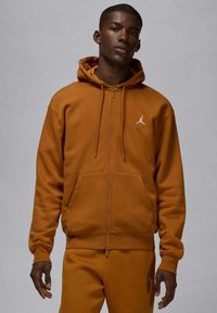 Felpa con cappuccio marrone con cerniera realizzata in tessuto morbido, con una tasca a marsupio e un piccolo logo Jumpman bianco sul petto a sinistra.