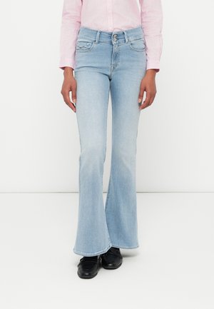 Jean évasés bleu clair en denim, dotés d'une taille haute, de cinq poches et d'un léger délavage, associés à des chaussures noires et une chemise rayée.