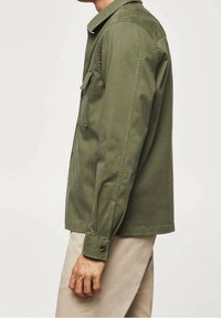 Oliivinvihreä pitkähiha-paita, jossa on terävä kaulus, yksi rintatasku, napilliset hihansuut ja rento istuvuus. Puuvillakangas, jossa sileä pinta.