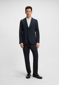 Navy suit with a fitted design, single button closure, notch lapels, and two front pockets. Styled with a white shirt and black shoes.
