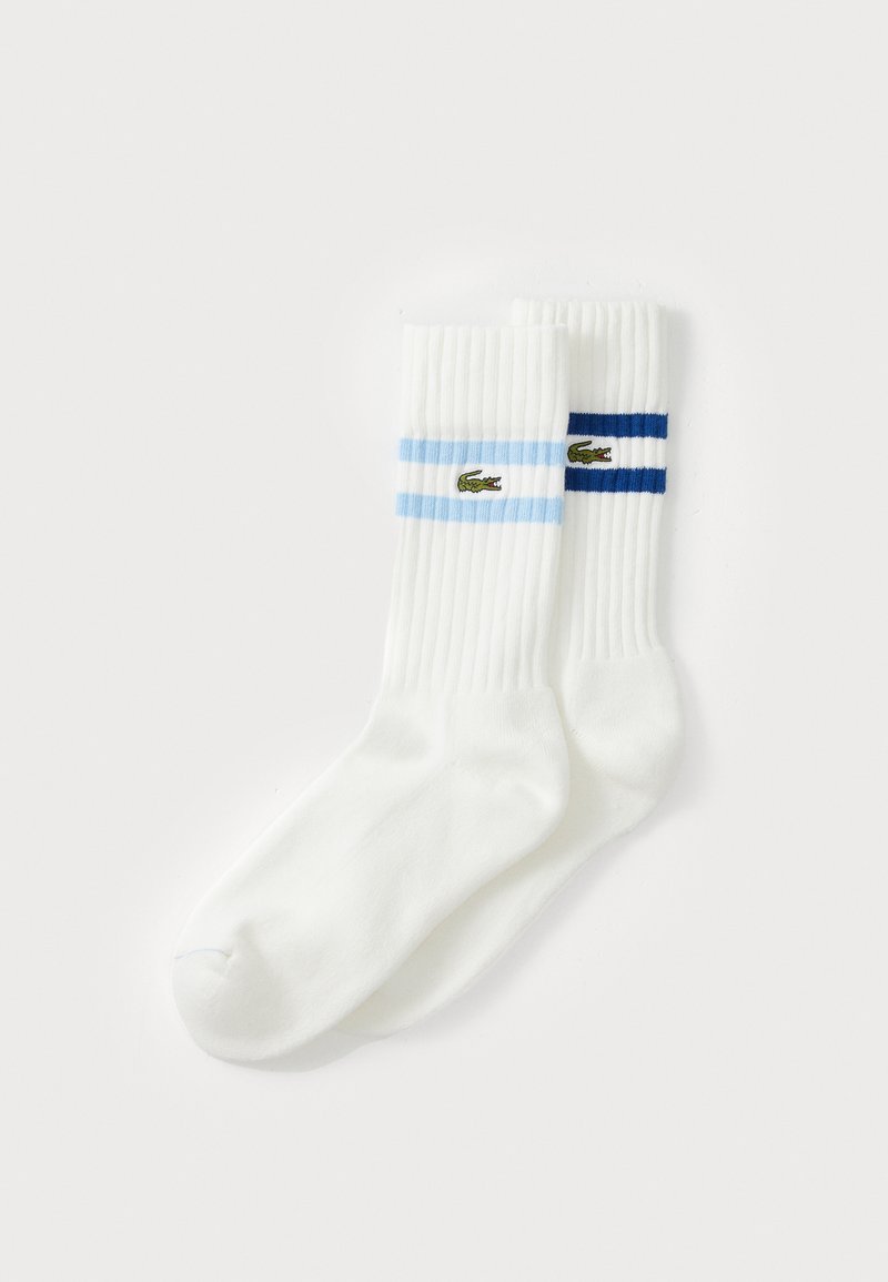 Chaussettes blanches côtelées avec des rayures bleu clair et bleu foncé, ornées d'un petit logo de crocodile brodé en vert sur les rayures.