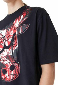 Maglietta nera con una grande grafica di un toro marmorizzato rosso e bianco sul fronte. Maniche corte e scollatura rotonda classica.