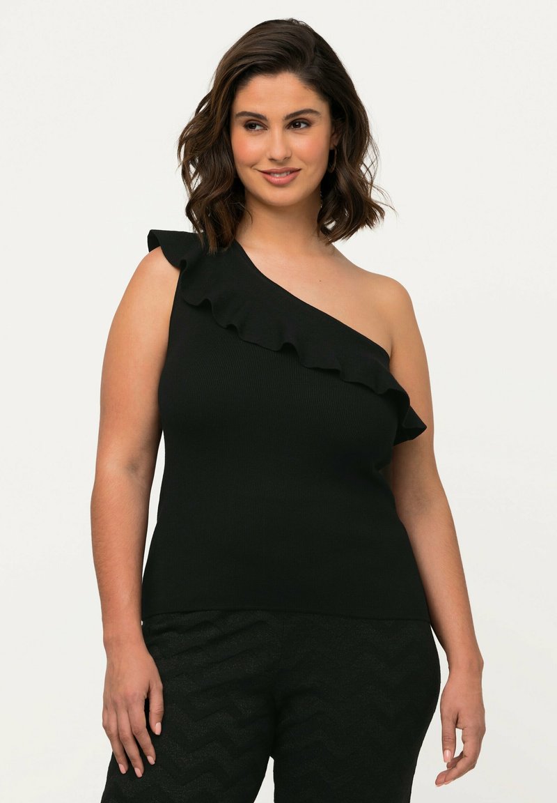 Sort ribbet top med design der går over den ene skulder og flæse detaljer. Stoffet er glat med en tætsiddende silhuet. Bæres med strukturerede sorte bukser.
