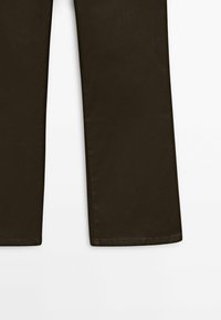 Gros plan sur les extrémités inférieures d'un pantalon brun foncé à coupe droite sur fond blanc, montrant la texture du tissu et les détails de la couture.