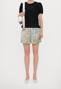 Top in pizzo nero con texture e maniche a sbuffo, abbinato a una gonna pastello con motivi di foglie di palma verdi. Borsa bianca con manici a righe.