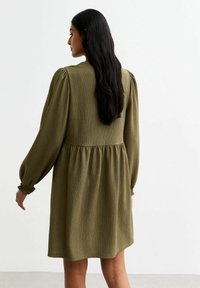Olive green dress with a textured fabric, long puffed sleeves, gathered waist, and a flared skirt, featuring elastic cuffs.