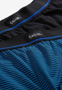Due paia di mutande da uomo, una nera uniforme e una blu con strisce nere, entrambe con fascia nera e etichette "CASUAL.".