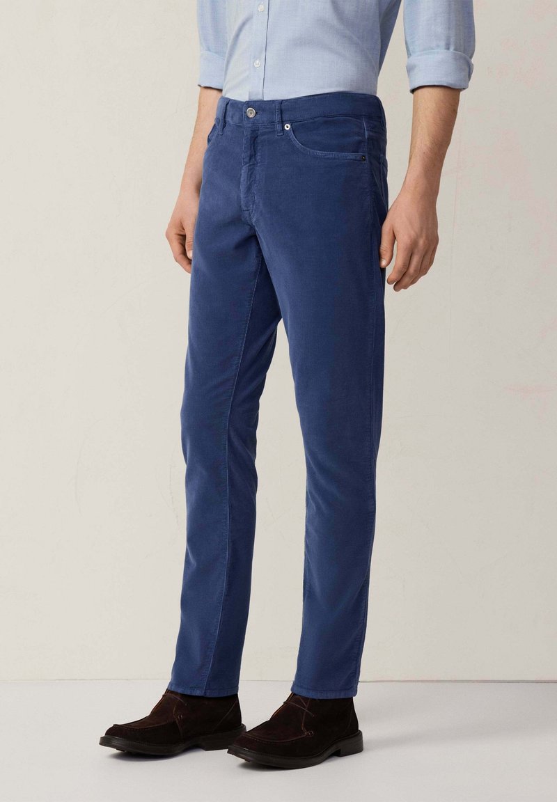 Blauwe corduroybroek met een slim fit, voorzien van een knoopsluiting, zijzakken en een subtiele textuur. Gecombineerd met donkerbruine enkellaarzen.