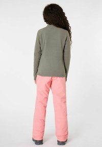 Chaqueta de forro polar en verde apagado, ajustada con mangas largas, combinada con pantalones de nieve impermeables en rosa. Tejido texturizado, corte relajado.