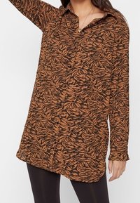 Camicia a maniche lunghe di colore marrone con un motivo astratto nero, dotata di colletto e chiusura con bottoni, realizzata in un tessuto testurizzato.