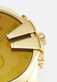 Orologio analogico in tonalità oro con un ampio quadrante giallo, marcatori delle ore audaci e distintivi dettagli in metallo. Resistente all'acqua fino a 10 bar.