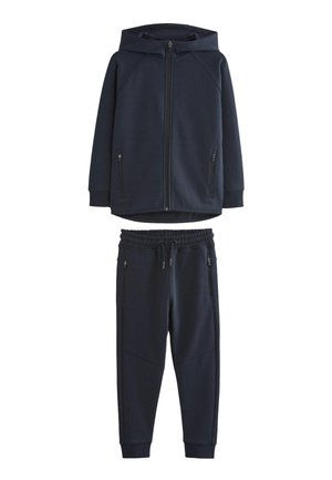 Tengerészkék melegítő kapucnis, cipzáras dzsekivel, cipzáras zsebekkel, és hozzáillő, elasztikus derékpántos, zsinórral és cipzáras zsebekkel ellátott melegítőnadrággal.