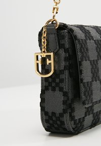 Czarna torebka w geometryczne wzory, wykonana z teksturowanej tkaniny, z złotym łańcuszkiem i okuciami oraz czarnymi, jednolitymi akcentami.