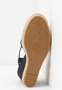Vue de dessous d'une sandale espadrille noire avec semelle tissée, semelle en caoutchouc, et logo Tommy Hilfiger sur la semelle.