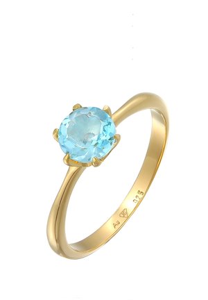 Anillo de oro con una piedra preciosa redonda de color azul claro sostenida por cuatro garras, grabado en el interior con "Ag 925" y una marca del fabricante.