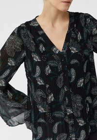 Czarna bluzka w kwiatowy wzór z akcentami w kolorze teal i białym. Plisowany materiał i dekolt w kształcie litery V. Długie, przezroczyste rękawy z elastycznymi mankietami.