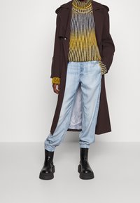 Brun lang frakke, stribed sweater i gul og grå, lyseblå jeans og sorte chunky støvler. Tekstureret materiale og afslappet pasform.