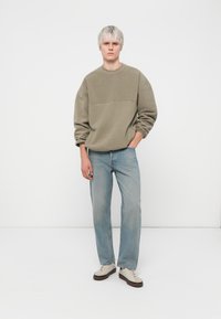 Olivenfarget hettegenser med teksturert design, kombinert med lyseblå jeans med rett ben og kremsnøringer med brune detaljer.