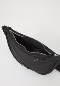 Svart nylon skulderveske med glidelås, som har en ytterlomme, glatt tekstur og minimalistisk design. Innvendig lomme synlig.