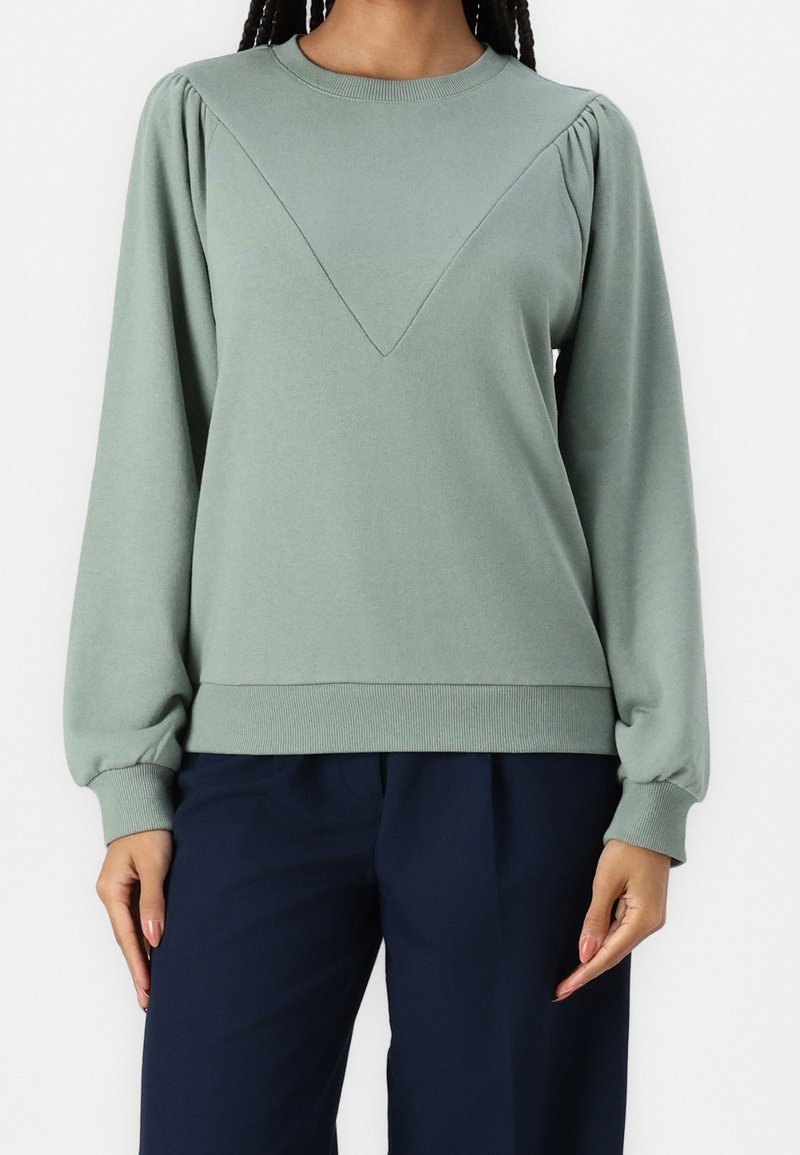 Sudadera verde menta con cuello redondo, que presenta mangas abullonadas con fruncidos y un diseño en forma de V en el frente. Puños y dobladillo acanalados.