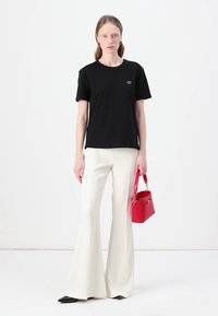 T-shirt en coton noir avec un petit emblème, associé à un pantalon froids blancs. Accessoire : sac à main rouge vif avec un design structuré.