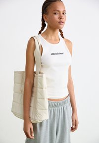 Hvid ribbet tanktop med "Dickies" trykt i sort. Grå sweatpants. Kræmfarget quiltet totebag med skulderrem og lynlås.