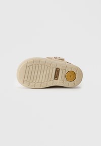 Lettvekts såle med en teksturert overflate, beige farge og et sirkulært logo accenter. Har spor og mønstre for grep.
