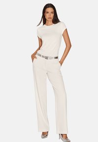 Witte aangesloten t-shirt gecombineerd met hoge taille, wijde crème broek. Voorzien van zilveren riem met logodetail en bijpassende metallic hakken.
