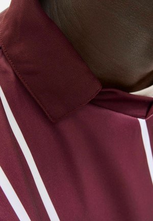 Gros plan sur une personne portant une chemise à col maroon avec des rayures blanches verticales et un col côtelé.
