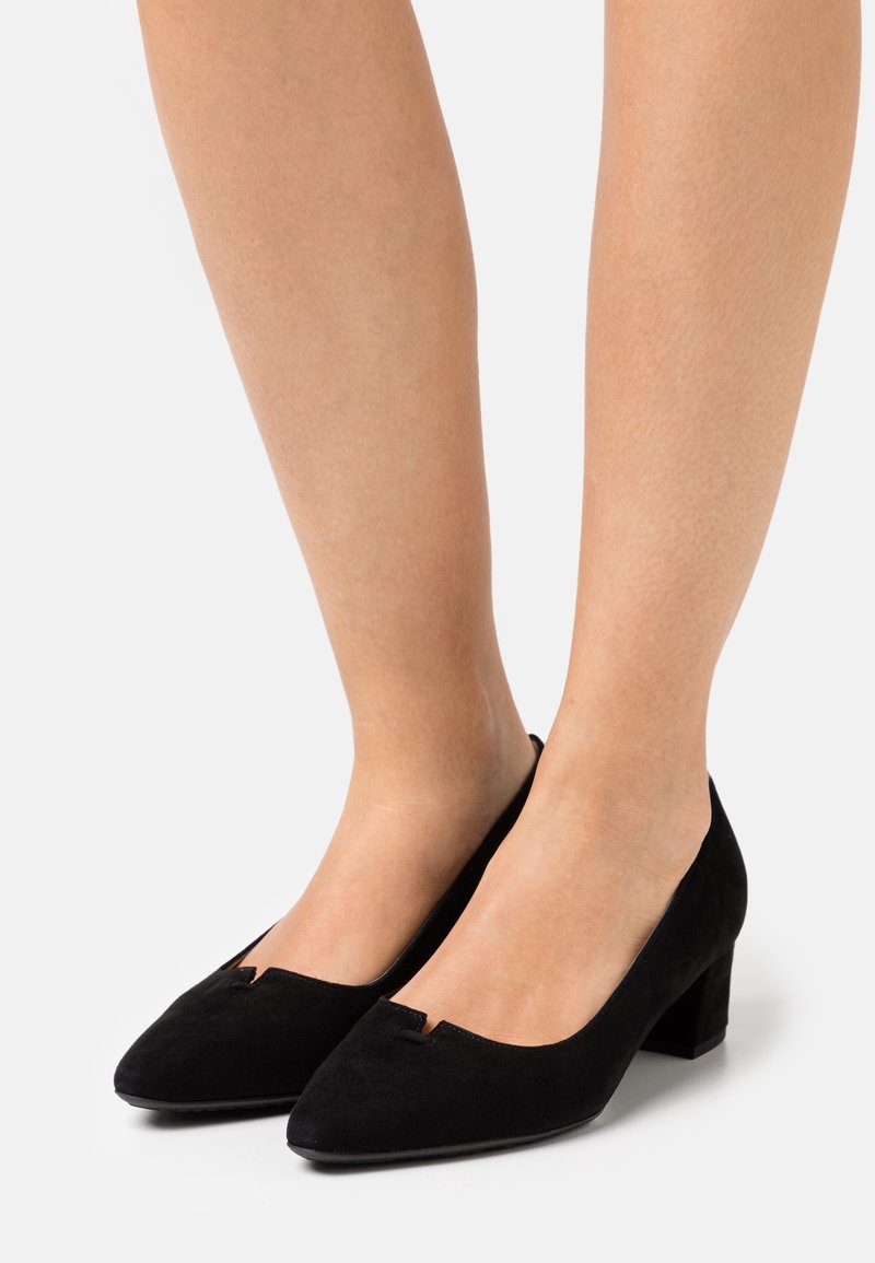 Zapatos de tacón bloque de ante negro con punta redonda y un pequeño detalle de corte en la parte superior. Textura suave y silueta clásica.