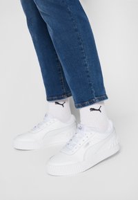 Vita Puma-sneakers i kombination med vita Puma-strumpor och blå jeans mot en enkel ljus bakgrund.