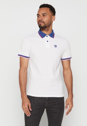 Camisa polo blanca con cuello azul y acentos rojos, con tapeta de dos botones y un logo bordado en el pecho. Mangas cortas.