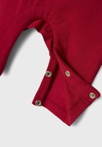 Rood katoenen kledingstuk met een ronde halslijn en drukknopen aan de zijkant. Soepele textuur met zichtbare stikseldetails.