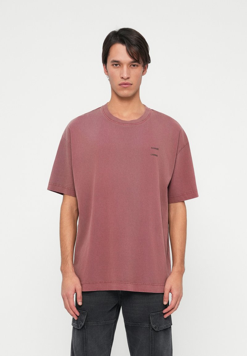 Kastmine, kulunud burgundia värvi T-särk, mis on valmistatud puuvillast, omab ümarat kaelust, lühikesi varrukaid ja rinnal väikest logo.