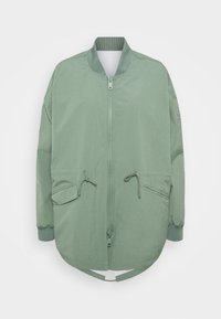 Jasnozielona kurtka bomberka z zamkiem z przodu, dwiema kieszeniami z klapami i sznurkiem, ściągaczem przy kołnierzu i mankietach oraz zaokrąglonym dołem.