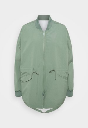 Jasnozielona kurtka bomberka z zamkiem z przodu, dwiema kieszeniami z klapami i sznurkiem, ściągaczem przy kołnierzu i mankietach oraz zaokrąglonym dołem.