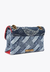 Borsa in denim con un motivo intrecciato intricato, caratterizzata da un design floreale blu, base in pelle rossa, accessori in oro e placca con logo.