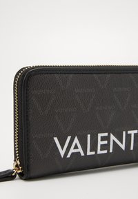 Black leather wallet featuring a gold zipper, embossed logo pattern, and a prominent white "VALENTINO" text on the front.