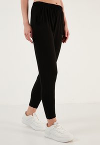 Zwarte elastische broek met zijzakken, tapered beenontwerp, gemaakt van een zachte, lichtgewicht stof. G gedragen met witte sneakers.