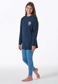 Navy long-sleeve shirt with graphic logo on chest paired with light blue leggings featuring a speckled pattern, worn barefoot.